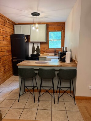 A compact kitchen with a central island, bar stools, a refrigerator, and a window. - Eagle's Nest | Riverfront Cabin Near Bryson City (Swain County)