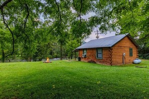 A wooden cabin with a metal roof, surrounded by a grassy yard and dense trees. - Eagle's Nest | Riverfront Cabin Near Bryson City (Swain County)
