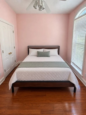 Une chambre à coucher avec un lit, un ventilateur de plafond, une fenêtre avec des stores et une porte.