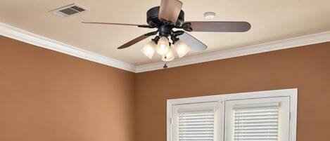 A dining room with a large wooden table surrounded by ornate chairs, a ceiling fan, and a door with white shutters.