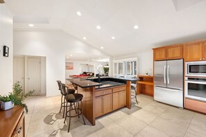 A modern kitchen with a central island, wooden cabinets, stainless steel appliances, and a dining area with bar stools. - 6BD/3.5BA Wine Country Home w/ Solar Heated Pool + Billiards + BBQ (Santa Rosa)
