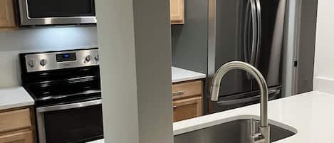 A modern kitchen with stainless steel appliances, wooden cabinets, and a white countertop.