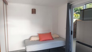 A small, single-bed room with a window, a wall-mounted light fixture, and a door leading to a balcony. - 'Aro'a Lodge: Exceptional views of the lagoon and Moorea (Faaa)