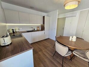Een moderne keuken met witte kasten, een houten aanrecht en een eetgedeelte met een ronde tafel en stoelen.