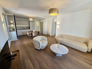 Een moderne woonkamer met een bank, twee fauteuils, een salontafel en een eethoek met een tafel en stoelen.