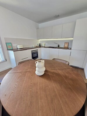 Una cocina moderna con armarios blancos, una mesa redonda de madera y un horno empotrado.