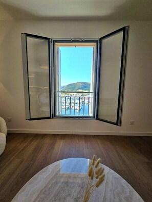 Una habitación con un ventanal grande, una mesa redonda de mármol y vistas a un puerto deportivo.