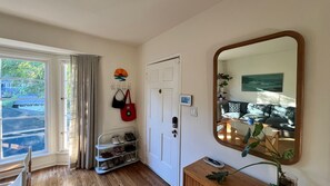 A room with a wooden floor, a white door with a keypad lock, a shoe rack, a mirror, and a window with curtains. - Charming 3 bed, 2 bath hillside home in Los Angeles. (Los Angeles)