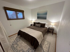 Un dormitorio con una cama, dos mesitas de noche, una ventana y un cuadro en la pared.