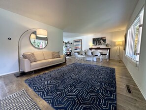 En moderne stue med sofa, et mønstret tæppe og et spiseområde med stole og et bord.