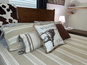 Ein Bett mit gestreifter Bettwäsche und mehreren Kissen, darunter eines mit einem Stier-Motiv und Text.