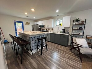 A modern kitchen with a central island, bar stools, and a dining area with a bench. - Tobin Hill Casita w/ Private Hot Tub near Pearl (San Antonio)