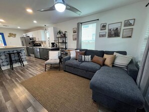Ein modernes Wohnzimmer mit einem grauen Ecksofa, einem kleinen weißen Sessel und einem gemusterten Teppich.