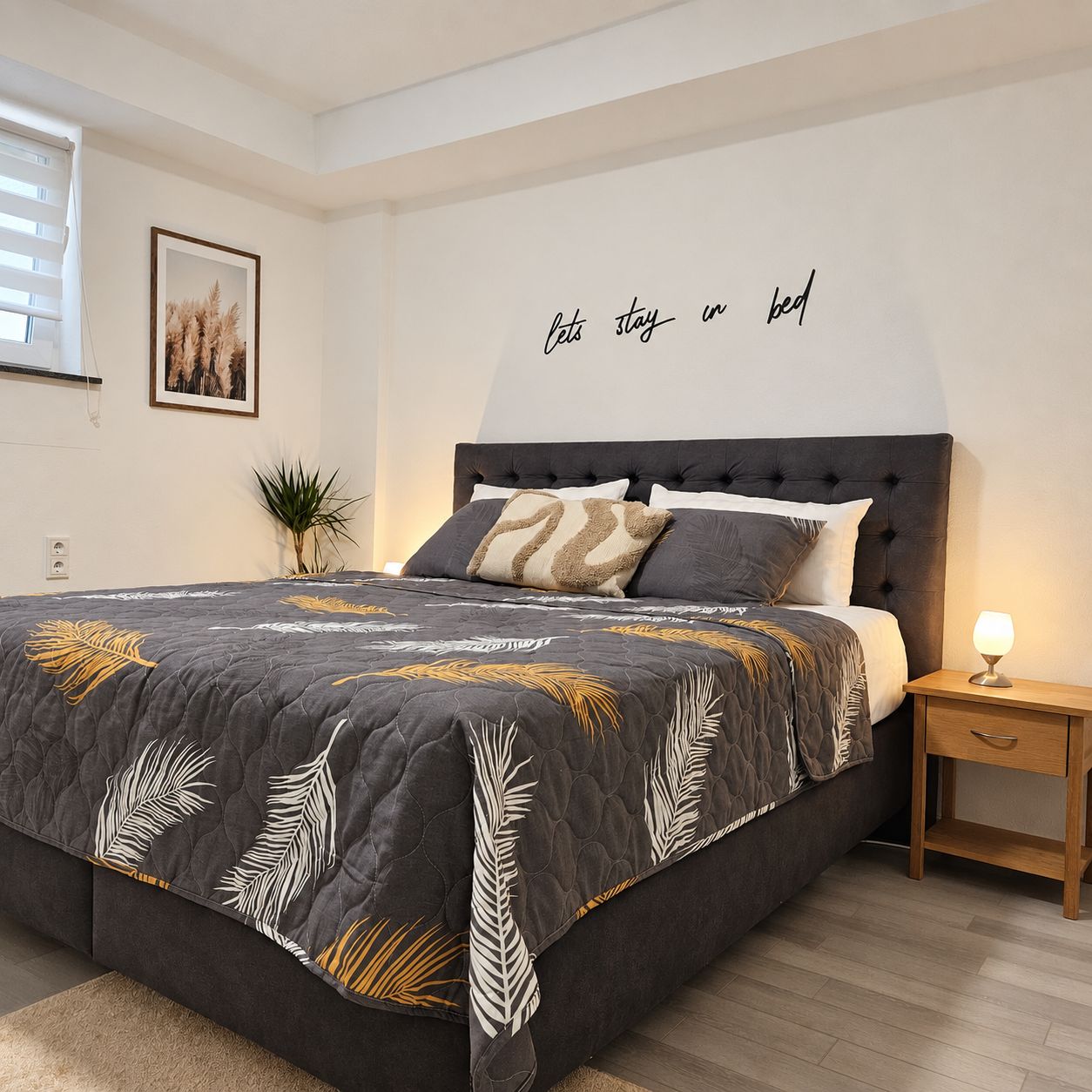 Une chambre à coucher avec un lit, une table de chevet, des œuvres d’art murales et une plante.