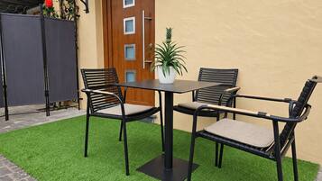 Une terrasse avec une table et quatre chaises, un pot de fleurs et une porte avec une fenêtre.