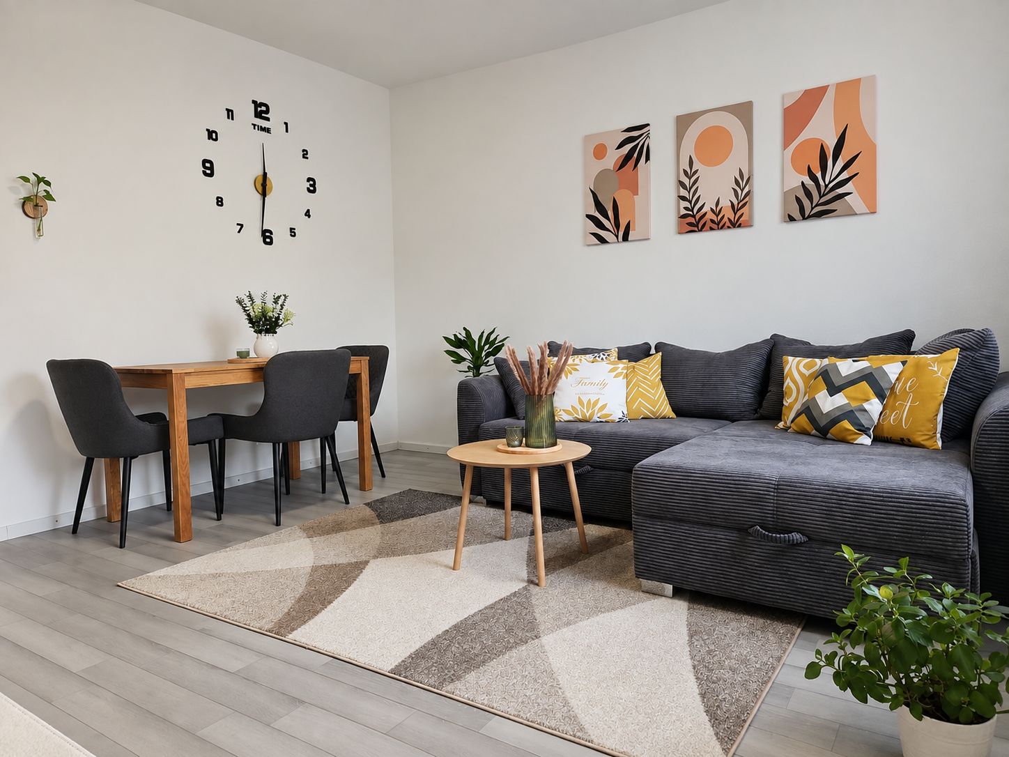 Ein modernes Wohnzimmer mit grauem Sofa, einem Esstisch mit Stühlen, einem Couchtisch und abstrakter Wandkunst.