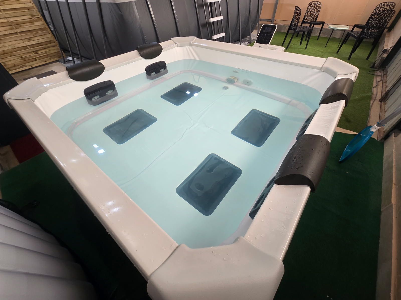 Een jacuzzi met vier jets, omringd door tuinmeubels en een vloer van groen kunstgras.
