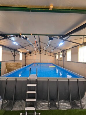 An indoor swimming pool with a ladder leading into the water, surrounded by a covered area with a roof structure. - Vrbo Property (Lublé)