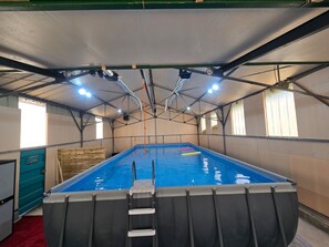 An indoor swimming pool with a ladder, surrounded by a covered area with metal beams and windows.