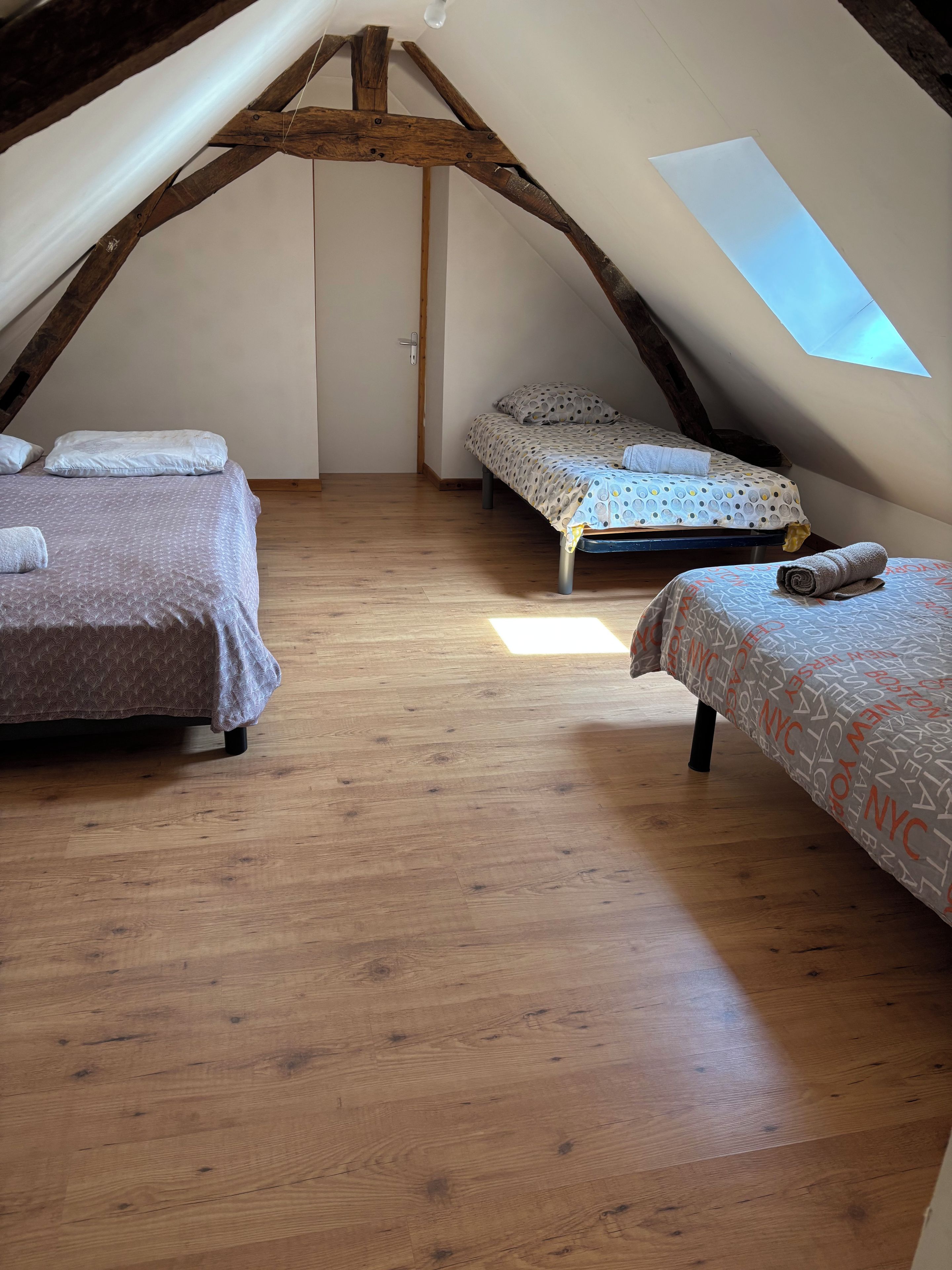 Une chambre à coucher aménagée dans un grenier, avec deux lits, des poutres en bois et une lucarne.