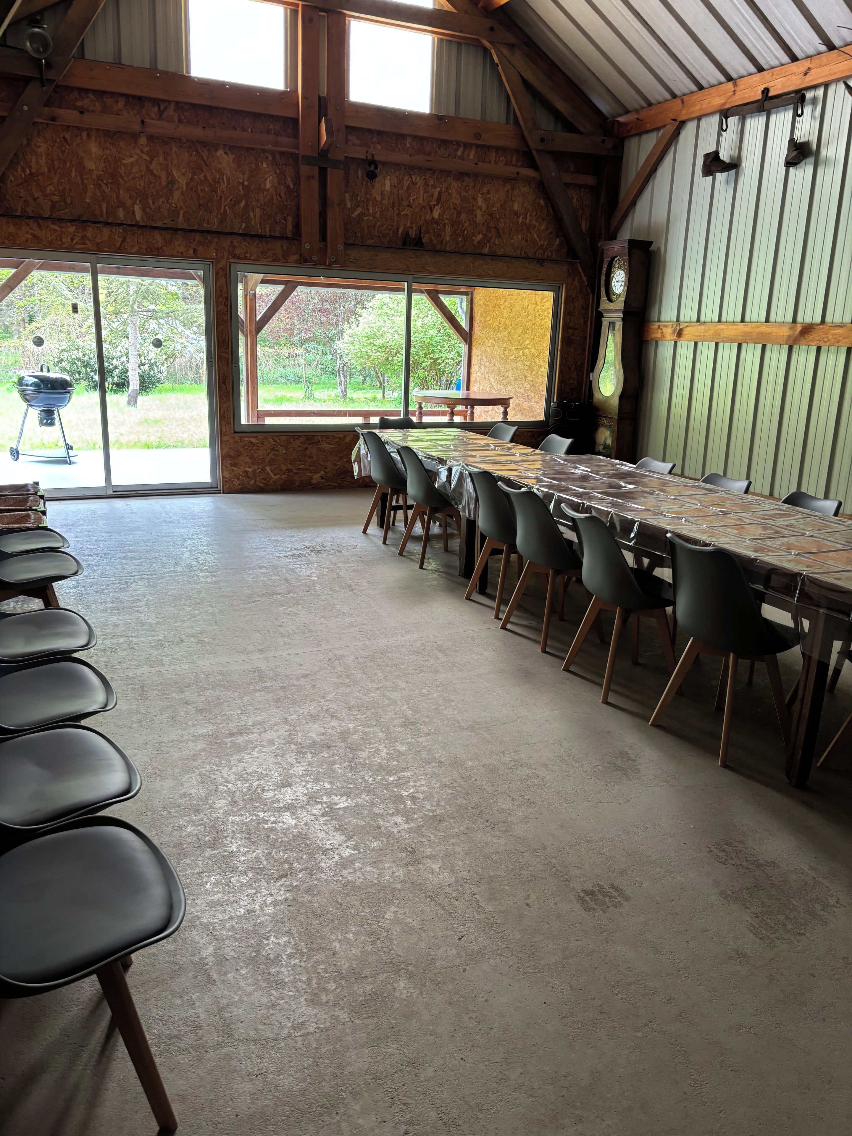 Een ruime eethoek met een lange tafel, meerdere stoelen, een houten plafond en uitzicht op groen.
