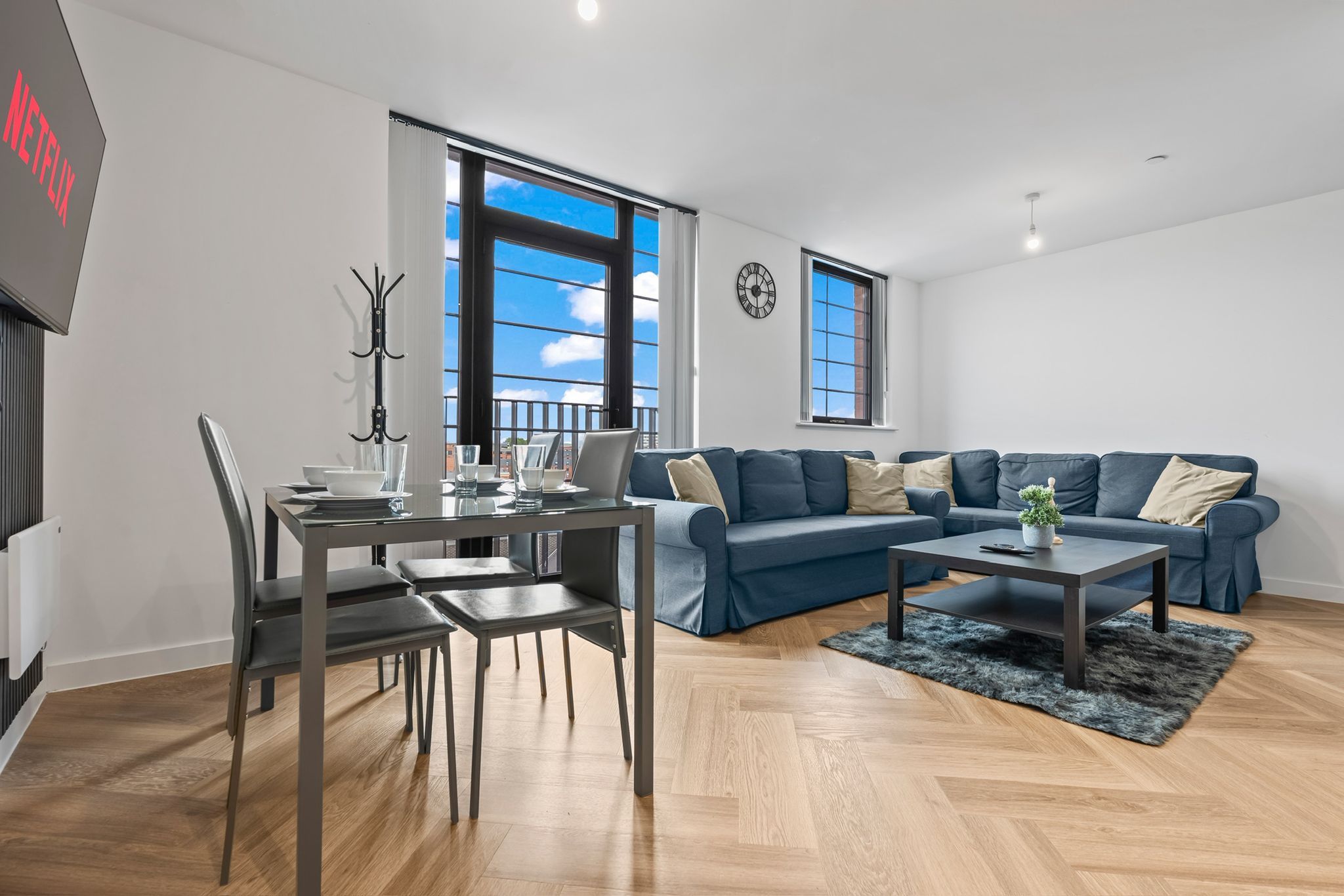 A modern living room with a dining area, a sofa set, a coffee table, and a TV mounted on the wall.