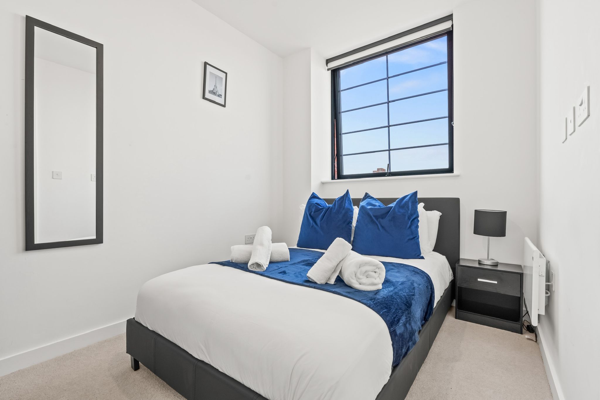 A modern bedroom with a bed, a nightstand, a window, and a framed picture on the wall.