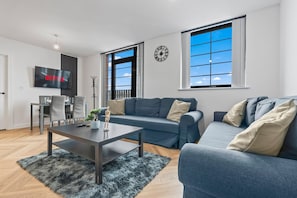 A modern living room with a sofa, a coffee table, a TV, and a large window. - Modern 2 Bed - Rooftop View - Central Birmingham (Birmingham)