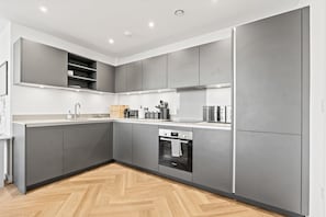 A modern kitchen with grey cabinetry, a Bosch oven, and a herringbone wooden floor. - Modern 2 Bed - Rooftop View - Central Birmingham (Birmingham)