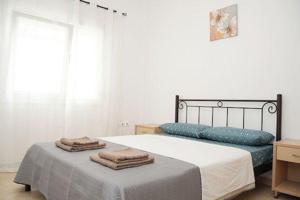 Un dormitorio con cama, dos mesitas de noche, una lámpara auxiliar y un cuadro colgado en la pared.