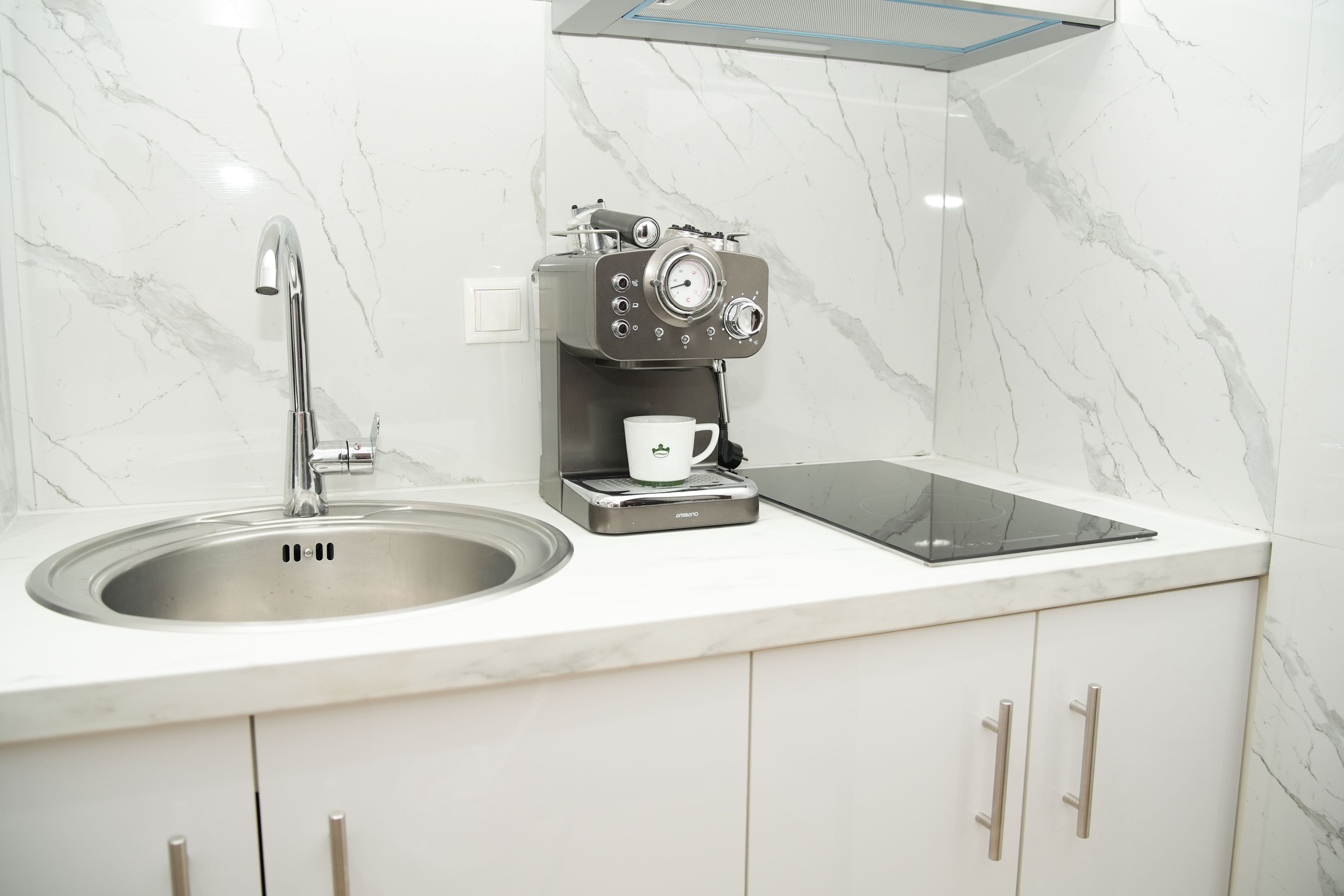 Una cocina moderna con un lavamanos de acero inoxidable, una cafetera y una cocina vitrocerámica empotrada.