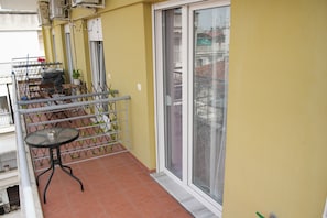 En balkon med gelænder, et lille rundt bord og en potteplante.