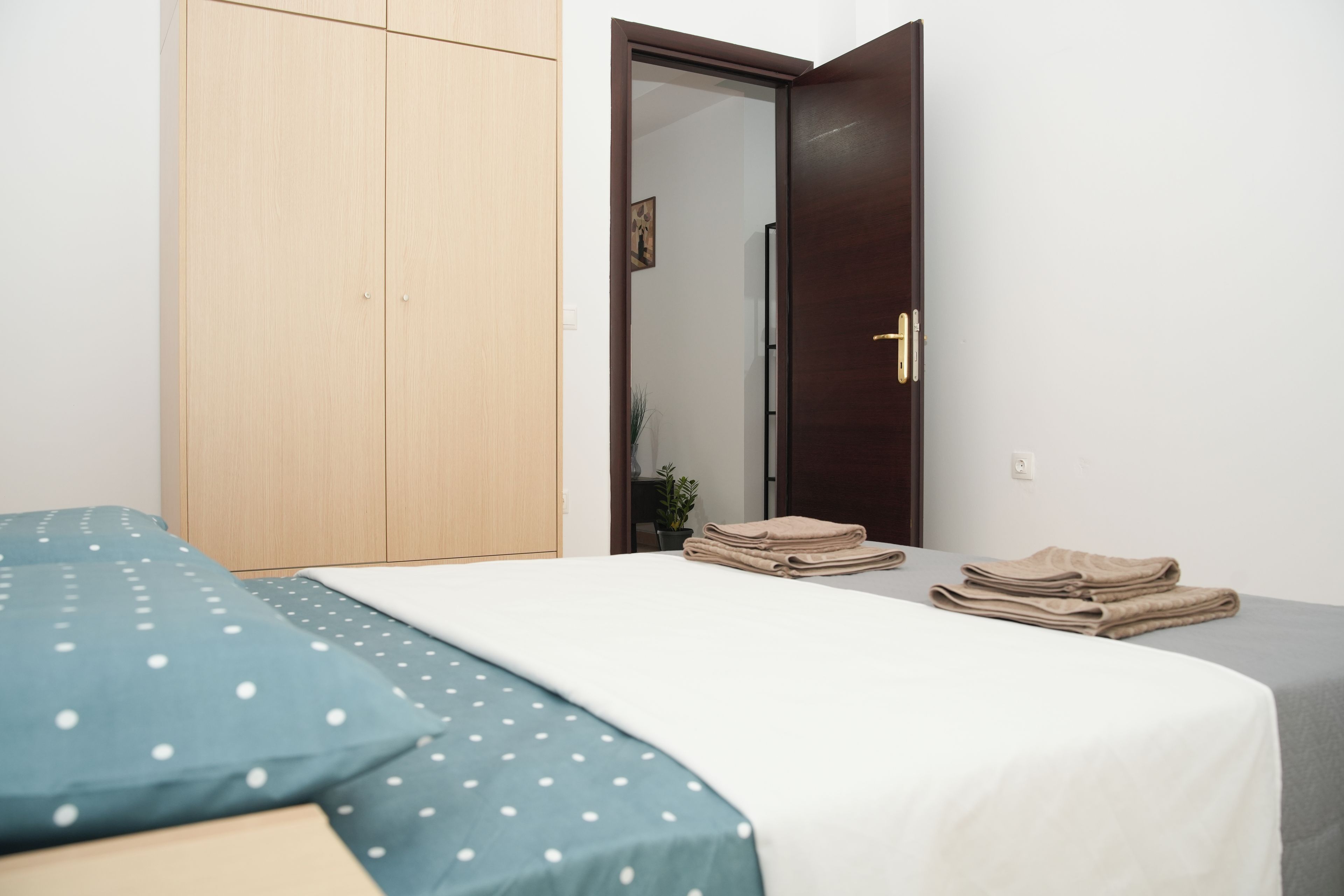 A bedroom with a bed, a wardrobe, a door, and a small table with folded towels.