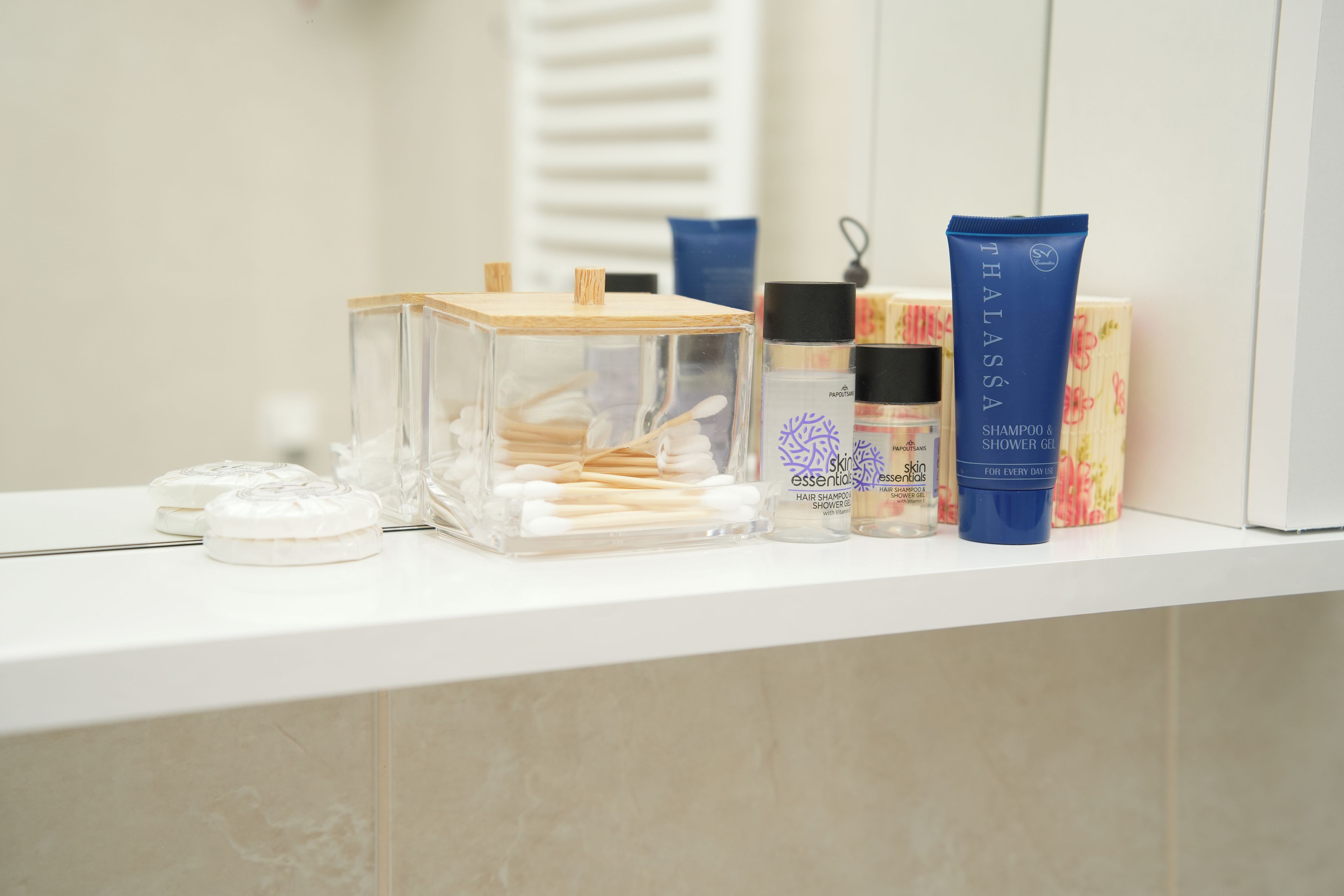 A bathroom vanity with toiletries including a clear glass container with cotton swabs, a blue tube of shampoo, and other personal care products.