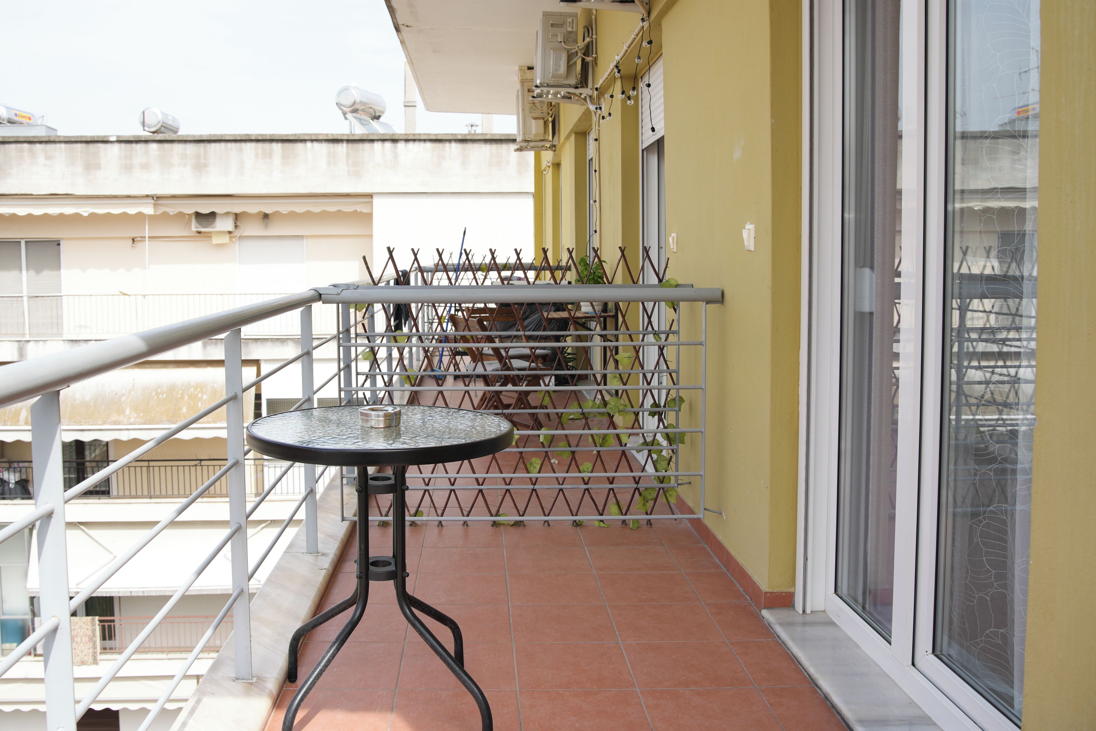 A balcony with a round table and chairs, a metal railing, and a view of a building in the background.