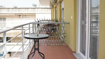 A balcony with a round table and chairs, a metal railing, and a view of a building in the background.