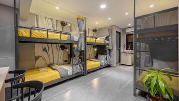 A bunk bed room with a desk and chair, a potted plant, and a kitchenette area.