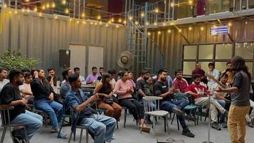 A group of people seated in a semi-circular arrangement in an indoor space with a high ceiling and industrial-style walls.
