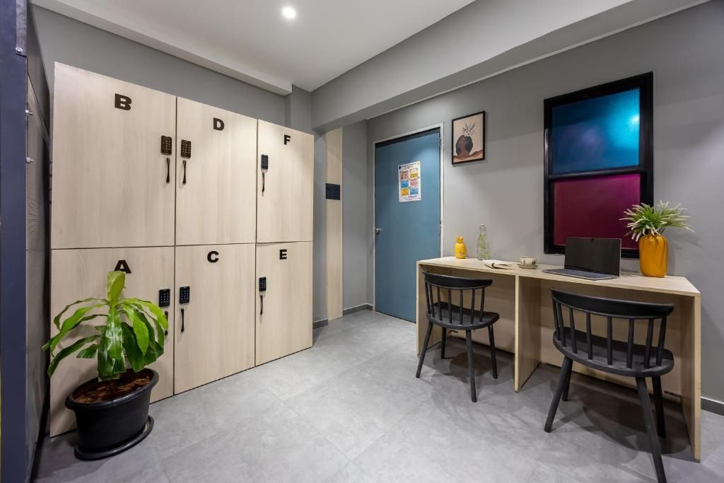 A hotel room with a desk, two chairs, a potted plant, a desk lamp, and a wall-mounted TV.
