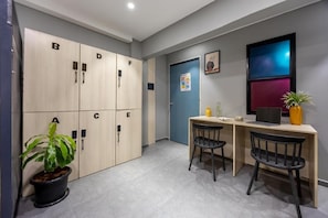 A hotel room with a desk, two chairs, a potted plant, a desk lamp, and a wall-mounted TV.