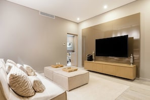 A modern living room with a sofa, ottoman, and a flat-screen TV mounted on a wooden cabinet. - Private Whirlpool Terrace - Gated 3BR Playacar, Beach + Town (Playa del Carmen)