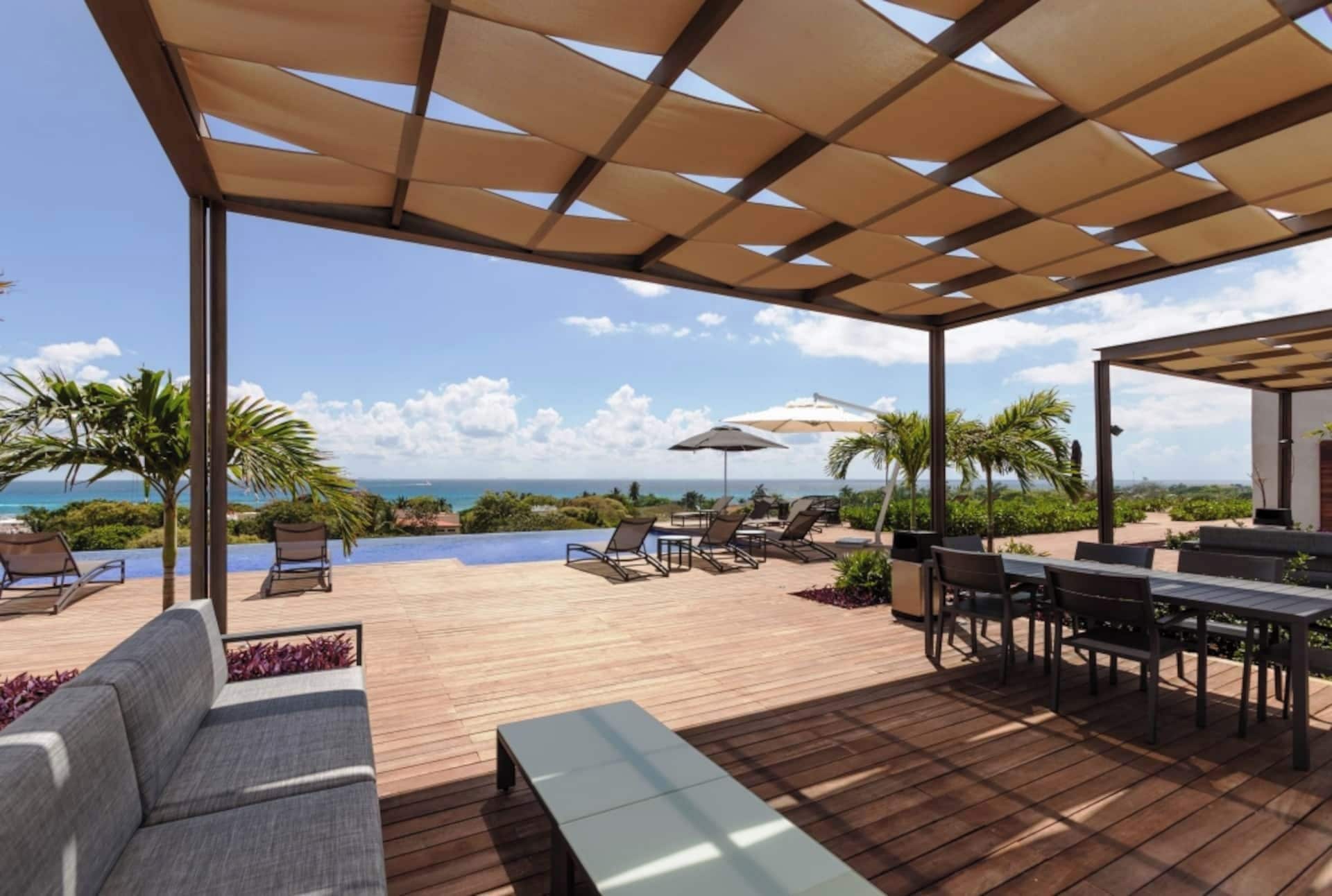 Une terrasse extérieure avec une plateforme en bois, des chaises longues, une piscine et une vue sur l’océan.