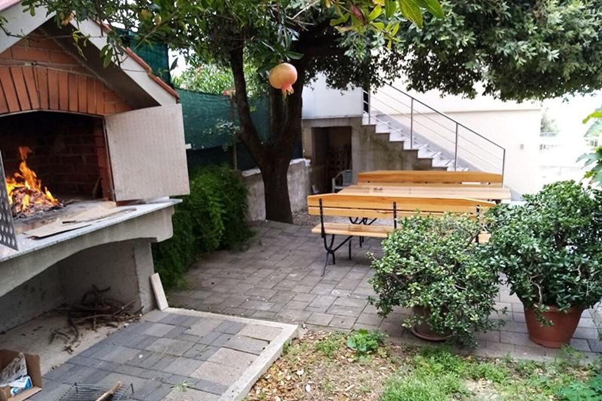 A backyard with a barbecue grill, a wooden bench, a potted plant, and a staircase leading to an upper level.
