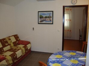 A room with a sofa, a dining table with a floral tablecloth, a painting on the wall, and a door leading to another room. - Villa Damir - Petrčane (Zadar)