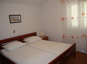 A double bed with a wooden headboard, a bedside table with a lamp, and a window with floral curtains. - Villa Damir - Petrčane (Zadar)