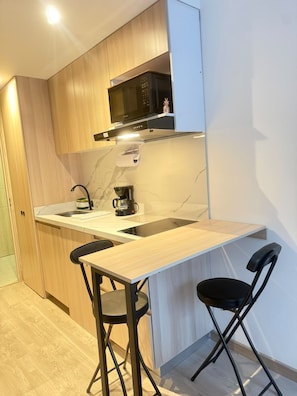 A compact kitchen with wooden cabinets, a microwave, a coffee maker, and a foldable dining table with two chairs. - Chicó Norte Gem, Walk to Parque 93 & Calle 100 (Bogotá)