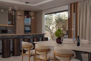 A modern dining area with a marble countertop, bar stools, and a table set for a meal. - Villa on Brač, 80 m from the sea, with a gym, a heated pool, a boat and driver (Splitska)