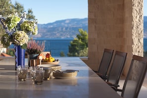 A table set with plates, glasses, and a fruit bowl, overlooking a scenic view. - Villa on Brač, 80 m from the sea, with a gym, a heated pool, a boat and driver (Splitska)