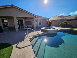 Une piscine résidentielle avec un jacuzzi encastré, un patio couvert et une maison avec un toit en tuiles.
