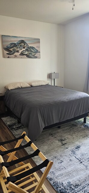 Een slaapkamer met een bed, nachtkastje, lamp, houten stoel en een schilderij aan de muur.